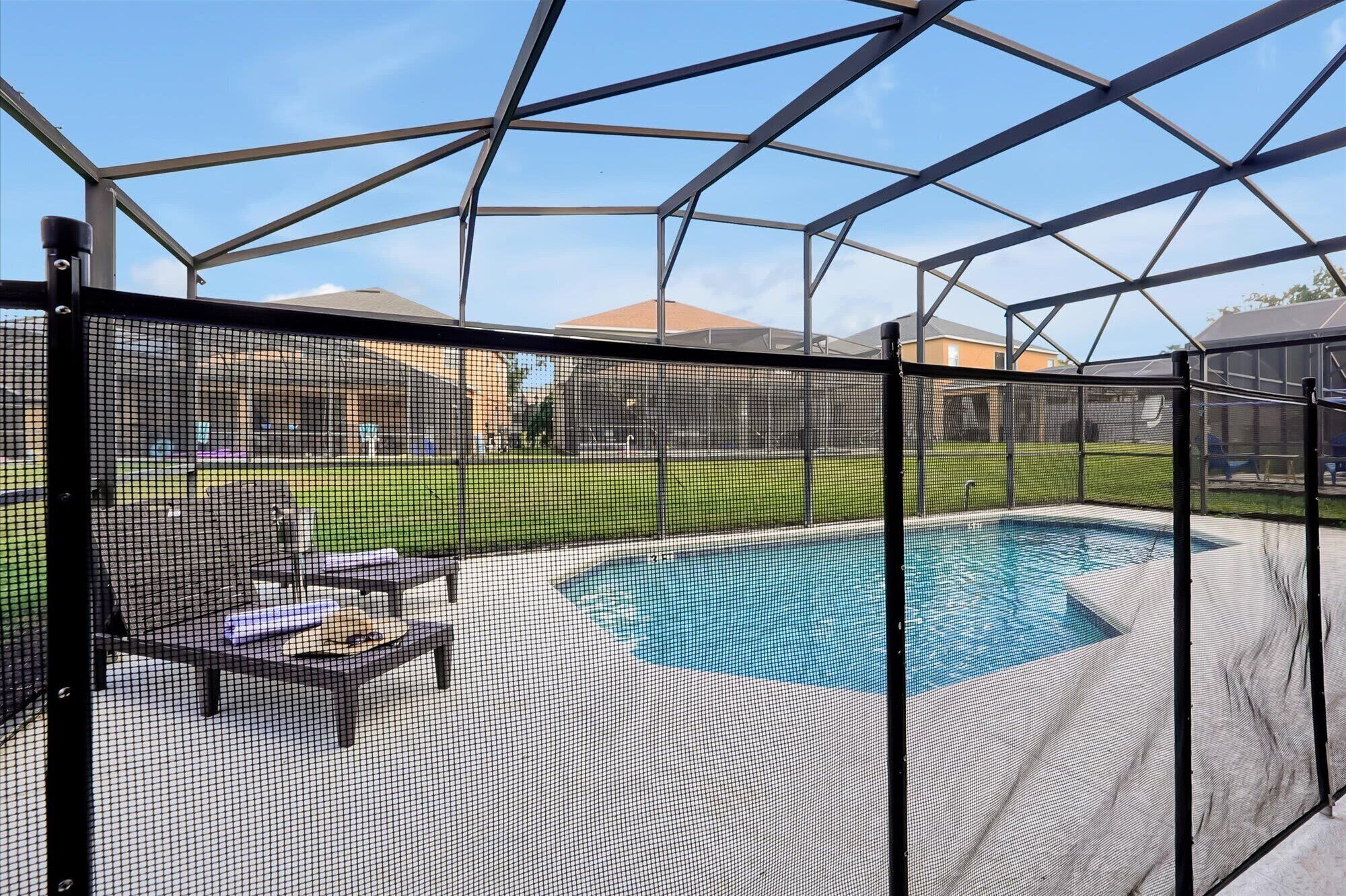 Piscina cubierta al aire libre con valla de seguridad, zona de patio con sillas y vistas a un barrio residencial.