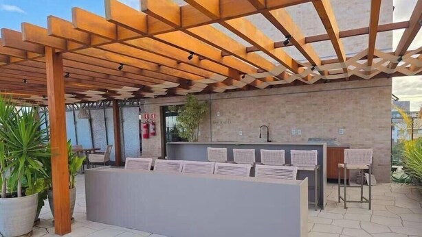 Ein überdachter Außenbereich mit einer Holzpergola, einer Theke mit Unterlagen und Topfpflanzen.