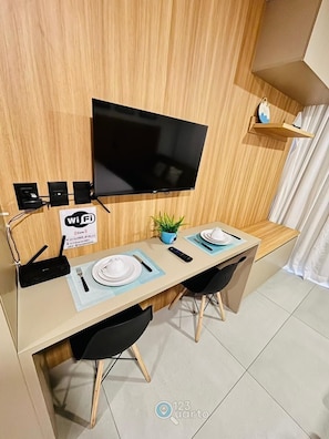 Un área de comedor moderna con una televisión de pantalla plana, un letrero de Wi-Fi y una planta pequeña.