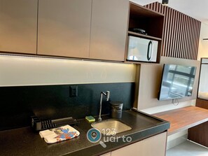 Una cocina moderna con microondas integrado, un lavamanos de acero inoxidable y una encimera de madera.