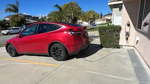 Une voiture rouge est garée dans l’allée d’une maison, à proximité d’une borne de recharge.