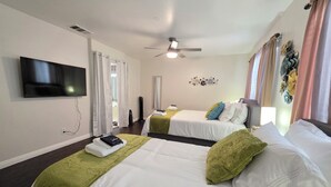 Habitación de hotel con dos camas, un televisor de pantalla plana, un ventilador de techo y un adorno de pared decorativo.