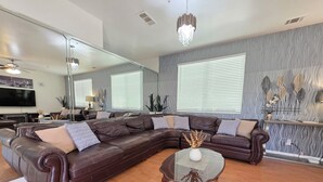Una sala de estar moderna con un amplio sofá modular, una mesa de centro de vidrio y un espejo decorativo.