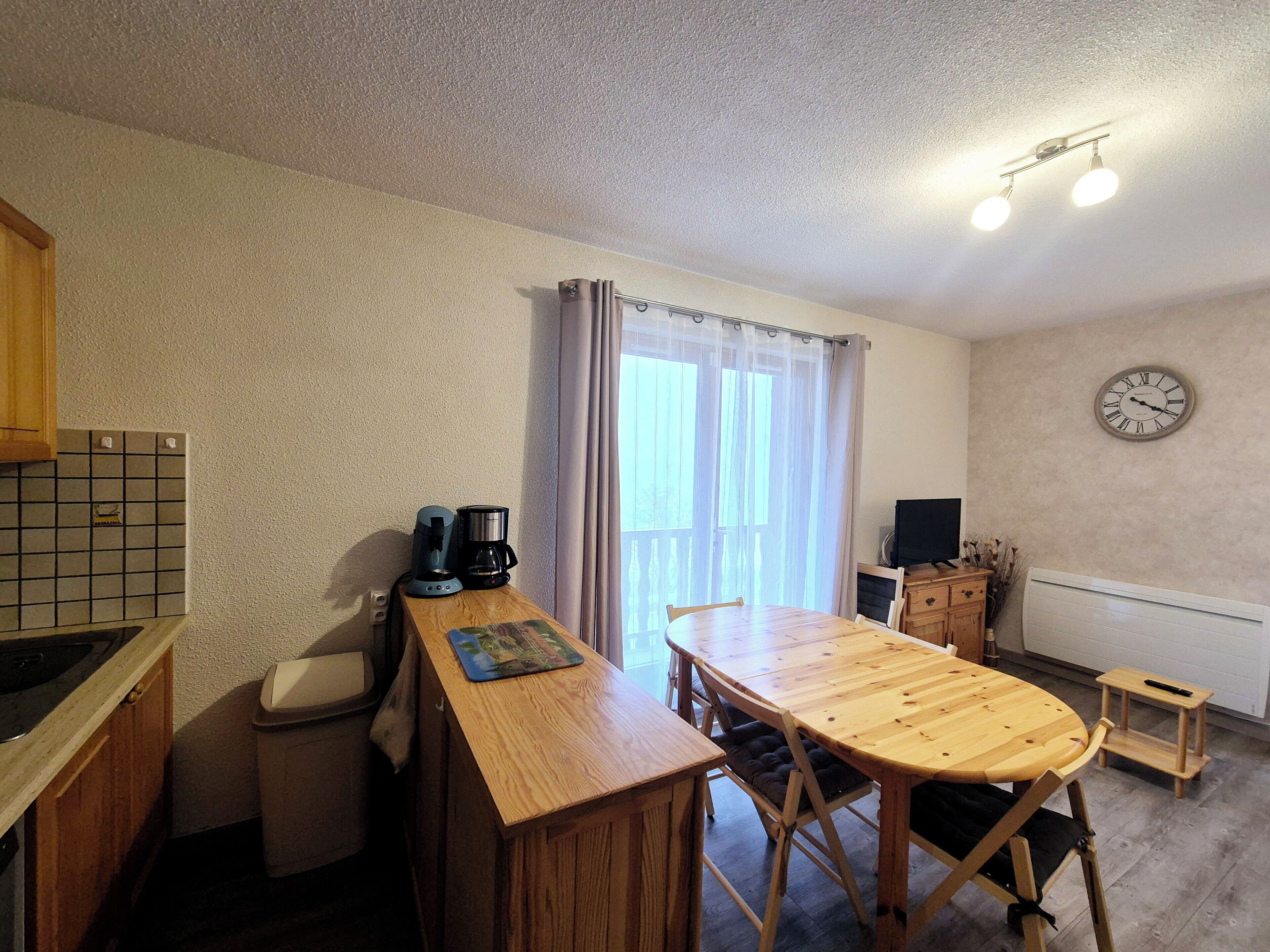 A compact kitchen with a wooden table, a coffee maker, and a clock on the wall.