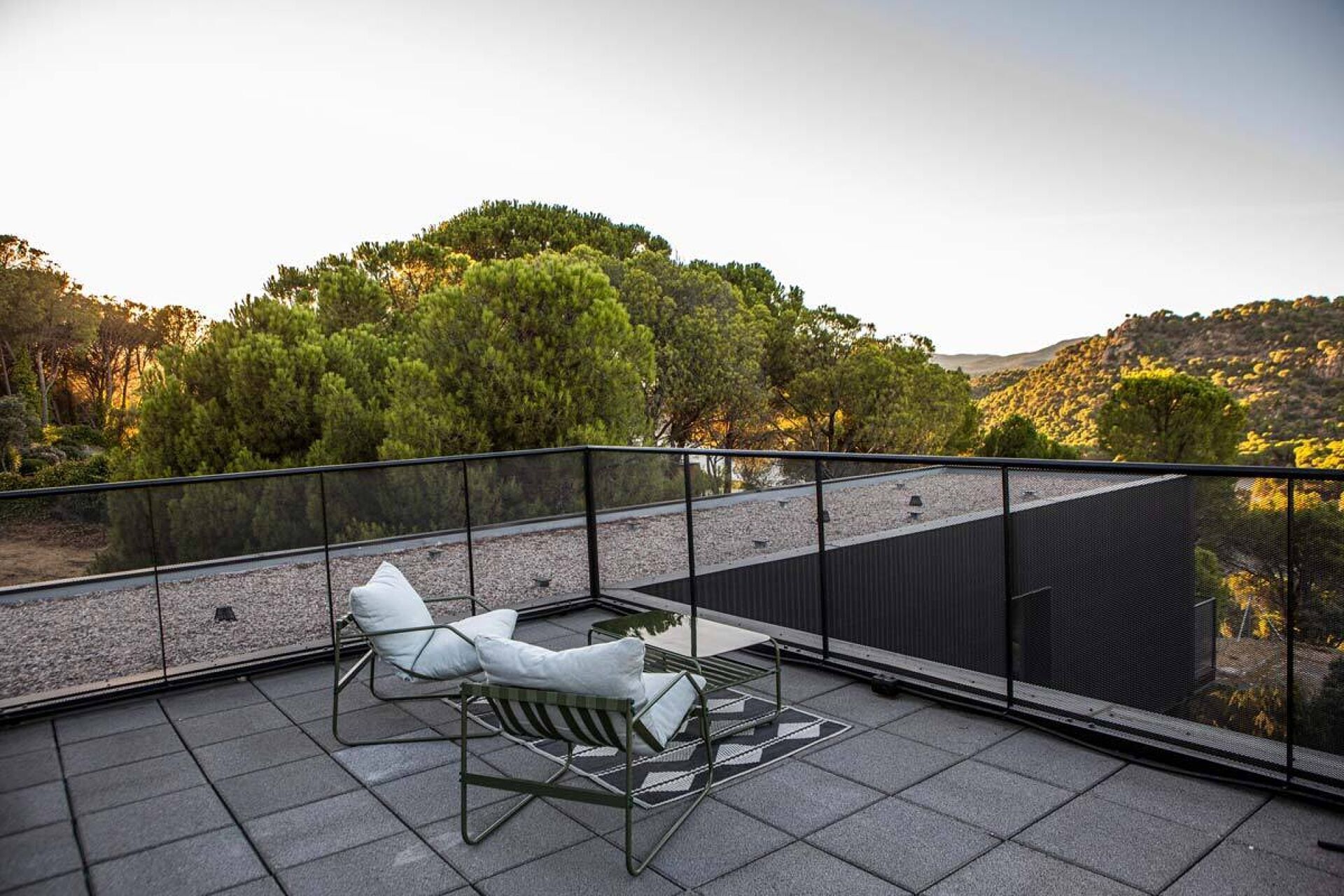 A rooftop terrace with two white lounge chairs and a view of a mountainous landscape.