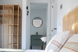 Een slaapkamer met een houten garderobe, een nachtkastje, een spiegel en een bed met gestreepte kussens.
