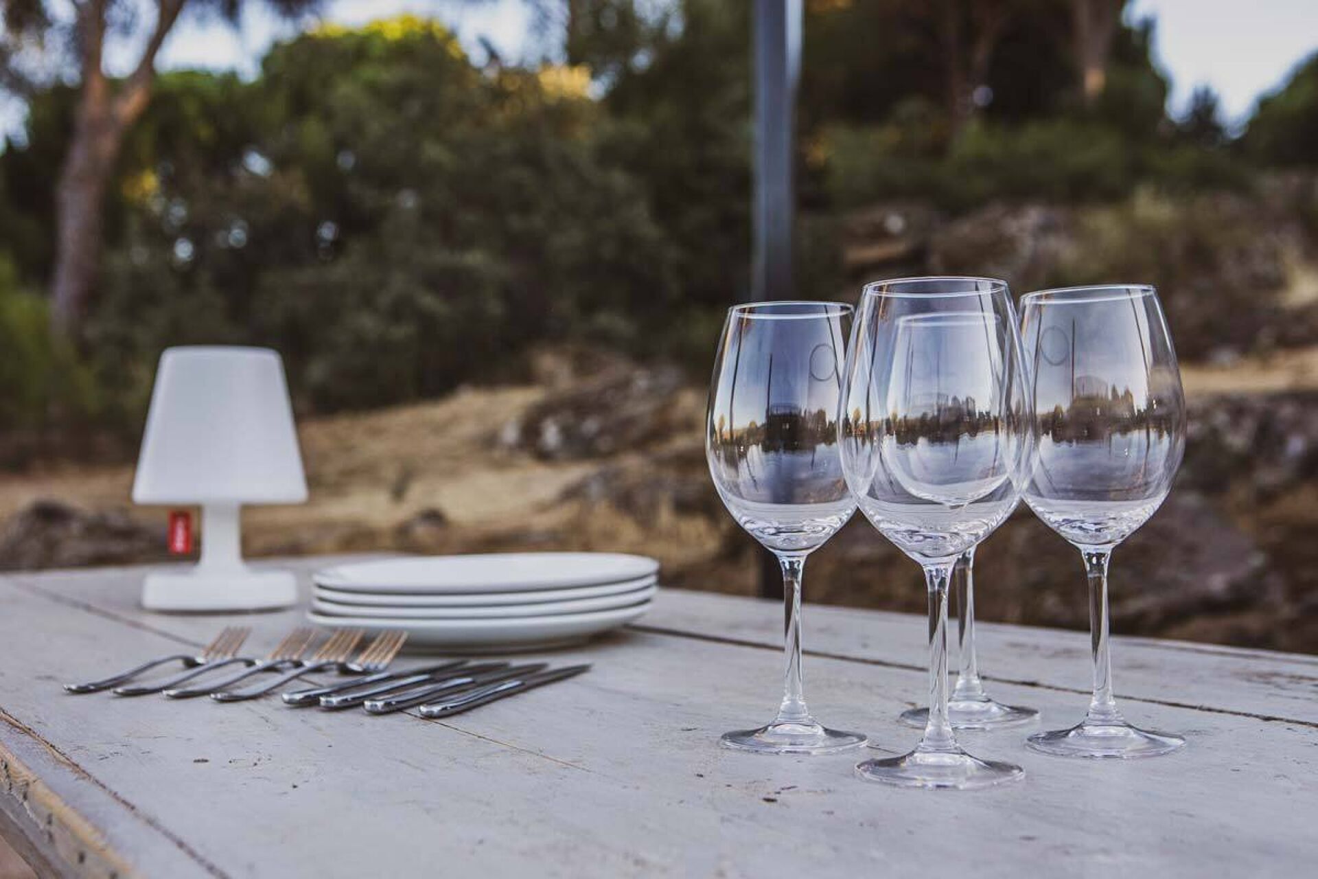 Une table avec quatre verres à vin, une pile d’assiettes blanches et un ensemble de couverts.