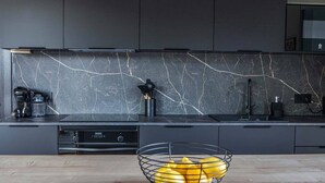 Una cocina moderna con salpicadero de mármol, cafetera y frutero sobre la encimera.