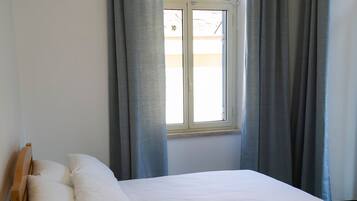 A single bed with white linens, a wooden headboard, and a bedside table with a lamp.