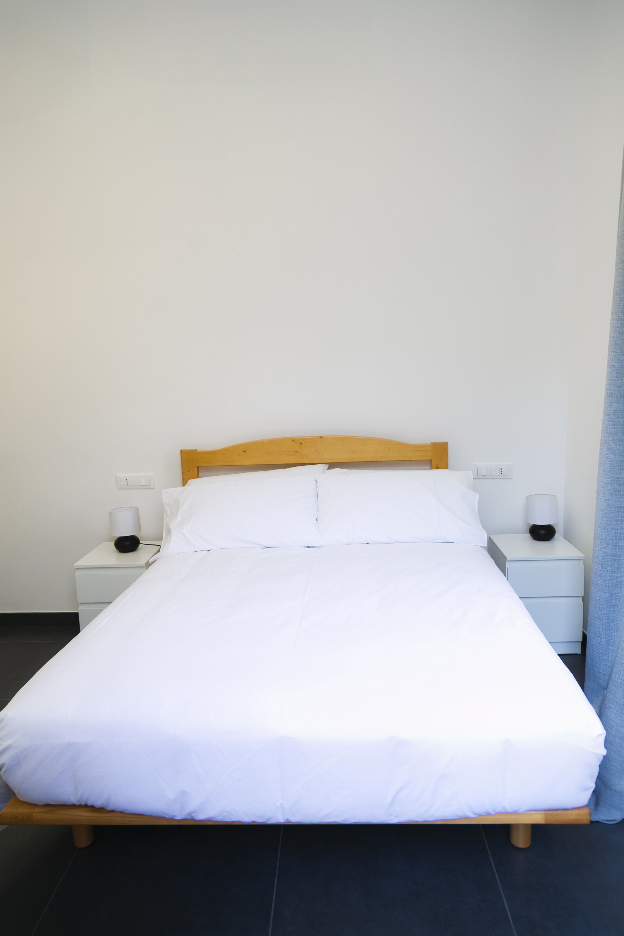 Una cama individual con cabecera de madera, ropa de cama blanca y dos mesitas de noche con lámparas.