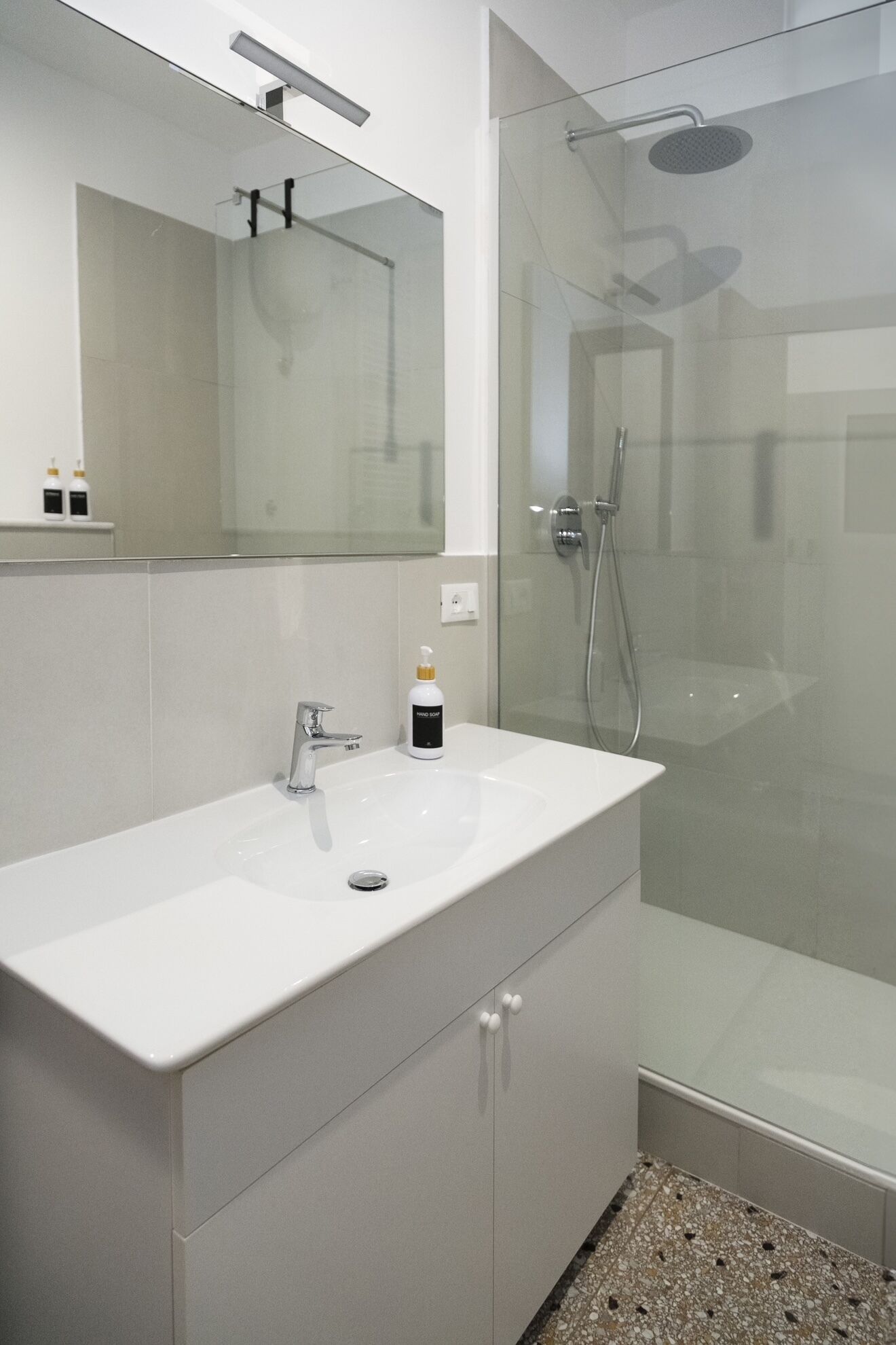A modern bathroom with a white vanity, a glass shower enclosure, and a mirror above the sink.