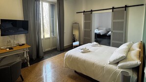 A hotel room with a bed, a desk, a TV, and a window with curtains. - la terrazza (Tivoli)