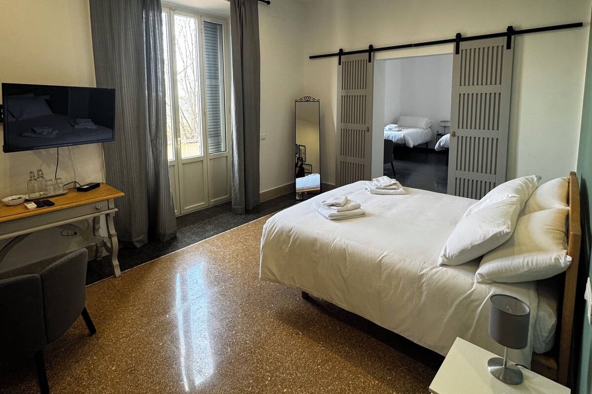 A hotel room with a bed, a desk, a TV, and a window with curtains.