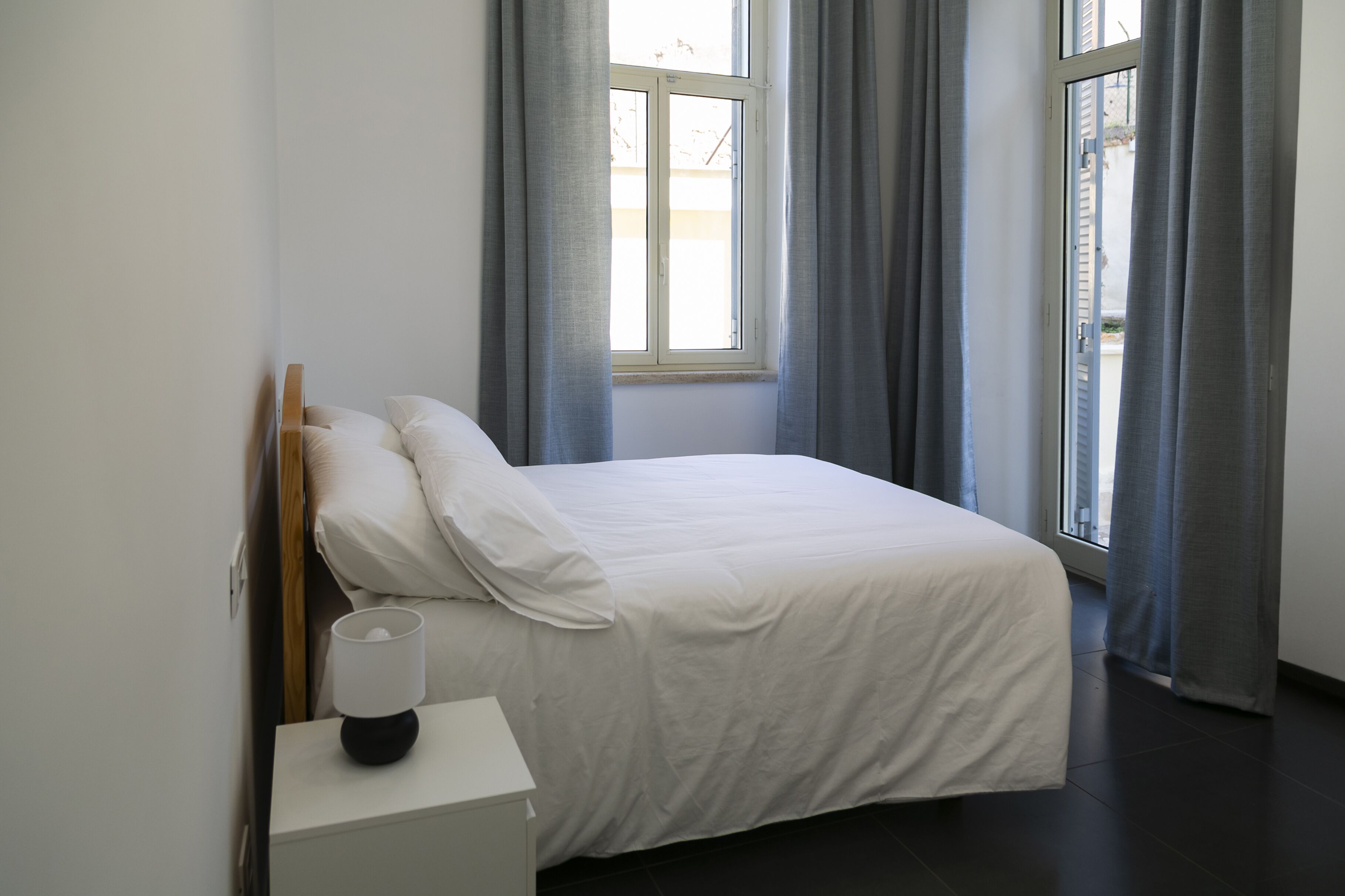 A bedroom with a bed, a bedside table with a lamp, and a window with curtains.
