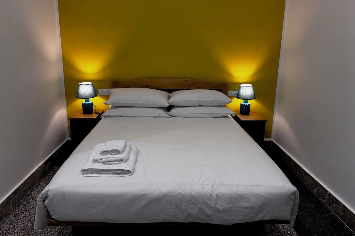 A neatly made bed with white linens and towels, two bedside lamps, and a wooden headboard.