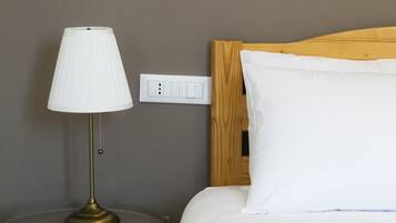 Hotellihuone, jossa on sänky, yöpöytälamppu ja pistorasia seinässä.