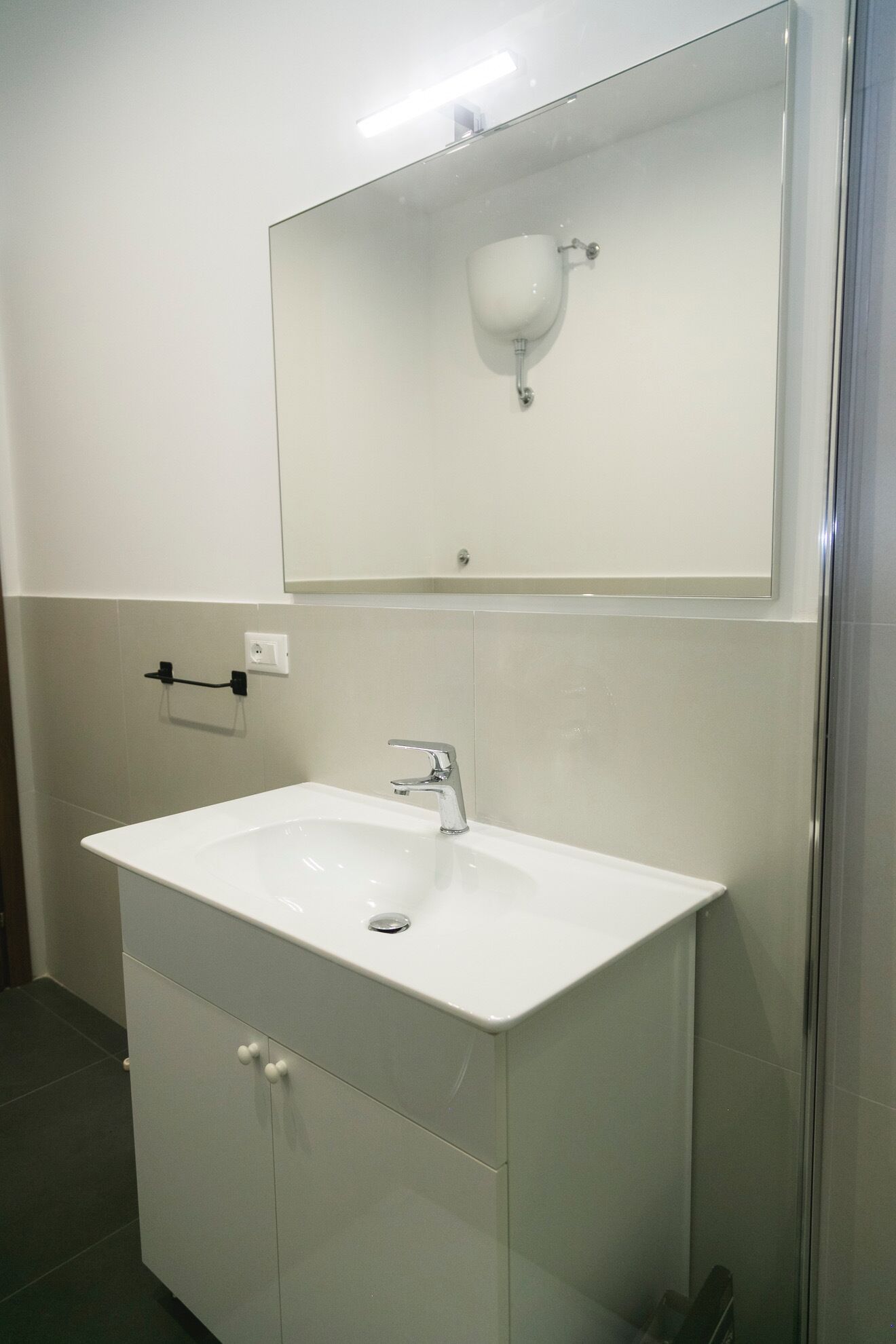A bathroom with a white sink, a mirror above it, and a towel rack to the left.