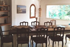 Un coin repas avec une table et des chaises en bois, une lampe et une fenêtre donnant sur un paysage verdoyant.