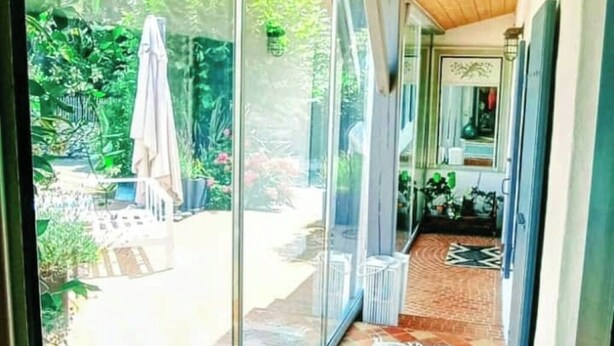 A glass door leading to a patio with a tiled floor, a white umbrella, and a brick pathway. - Artist's property/Pool 10X5/garden orchard (Rivedoux-Plage)