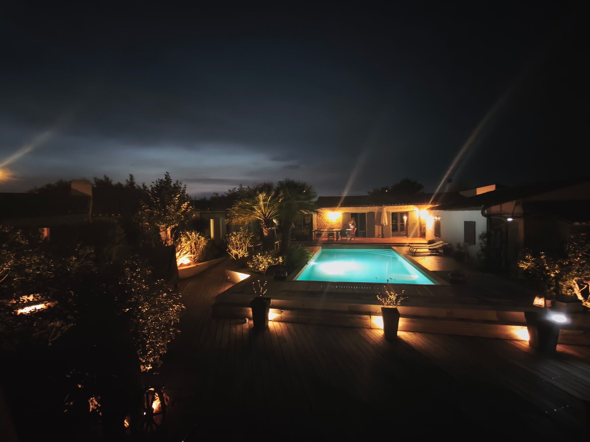 Ein Nachtblick auf einen Poolbereich mit einer Steinstruktur und Liegestühlen.