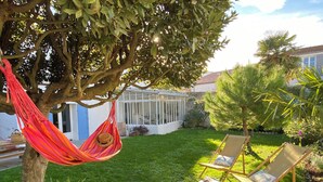 Ein Garten mit einer Hängematte, zwei Liegestühlen und einem Wintergarten.