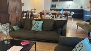 Ein gemütliches Wohnzimmer mit einem dunkelgrünen Sofa, einem Holztisch und einem Essbereich im Hintergrund.