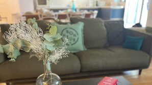 Ein Wohnzimmer mit Couchtisch, einer Vase mit getrockneten Pflanzen, einer kleinen Schale und einem Buch.