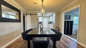 Een eetgedeelte met een lange tafel, donkere stoelen en een kroonluchter.