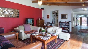 Un salón amplio con una pared de acento roja, vigas de madera, una chimenea y una estantería llena de libros.