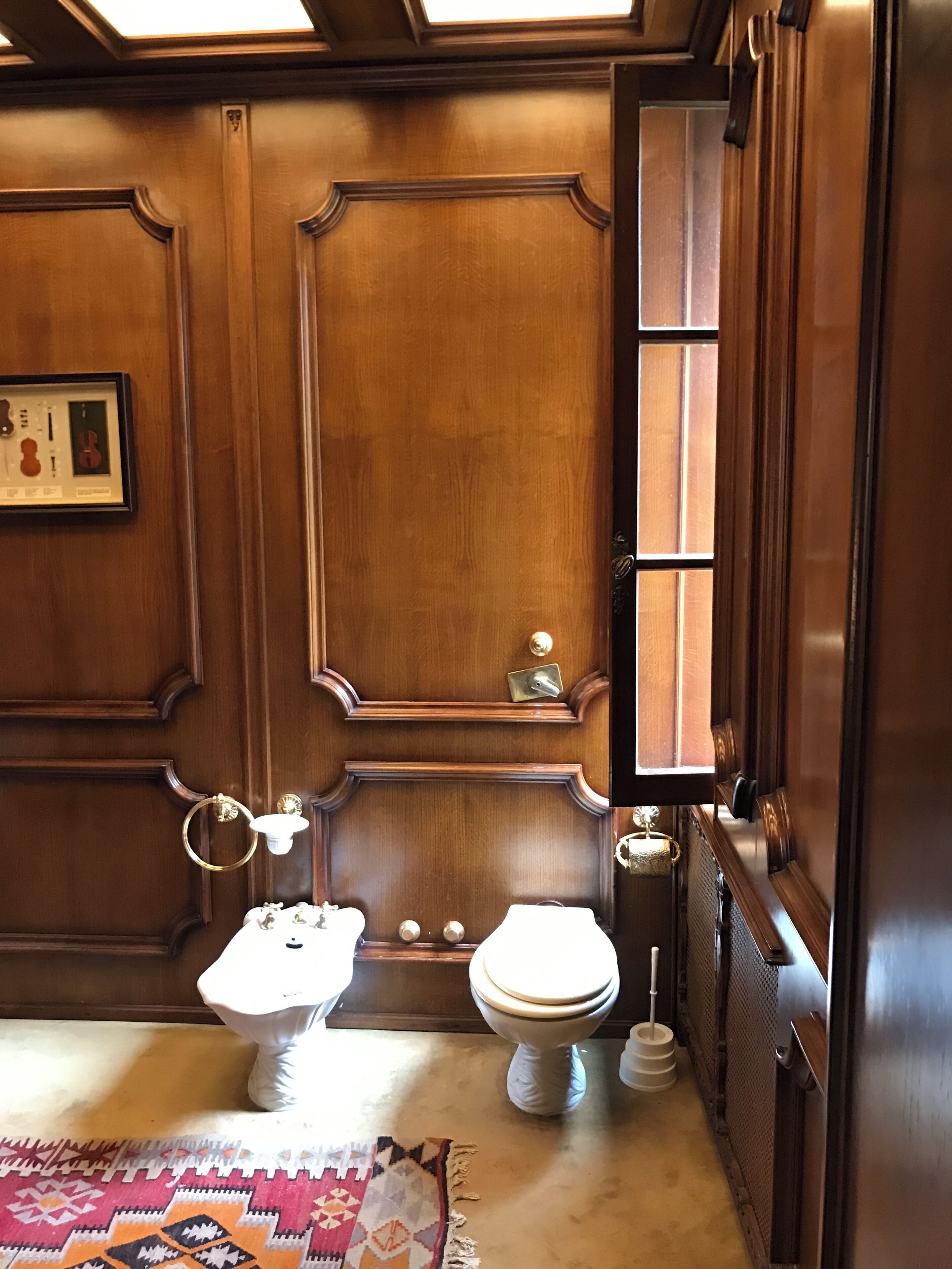A traditional bathroom with wooden paneling, a pedestal sink, a toilet, and a rug.