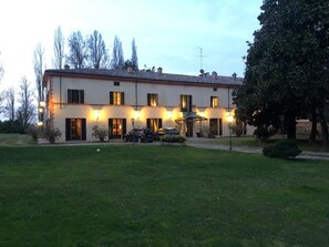 A two-story building with a flat roof and a balcony on the second floor. There are multiple windows on each floor, and the building is surrounded by a well-maintained lawn. - Villa Dom (Piacenza)