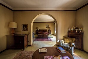 A hotel room with a bed, a sitting area with a table and armchairs, a dresser, and a lamp. - Villa Dom (Piacenza)
