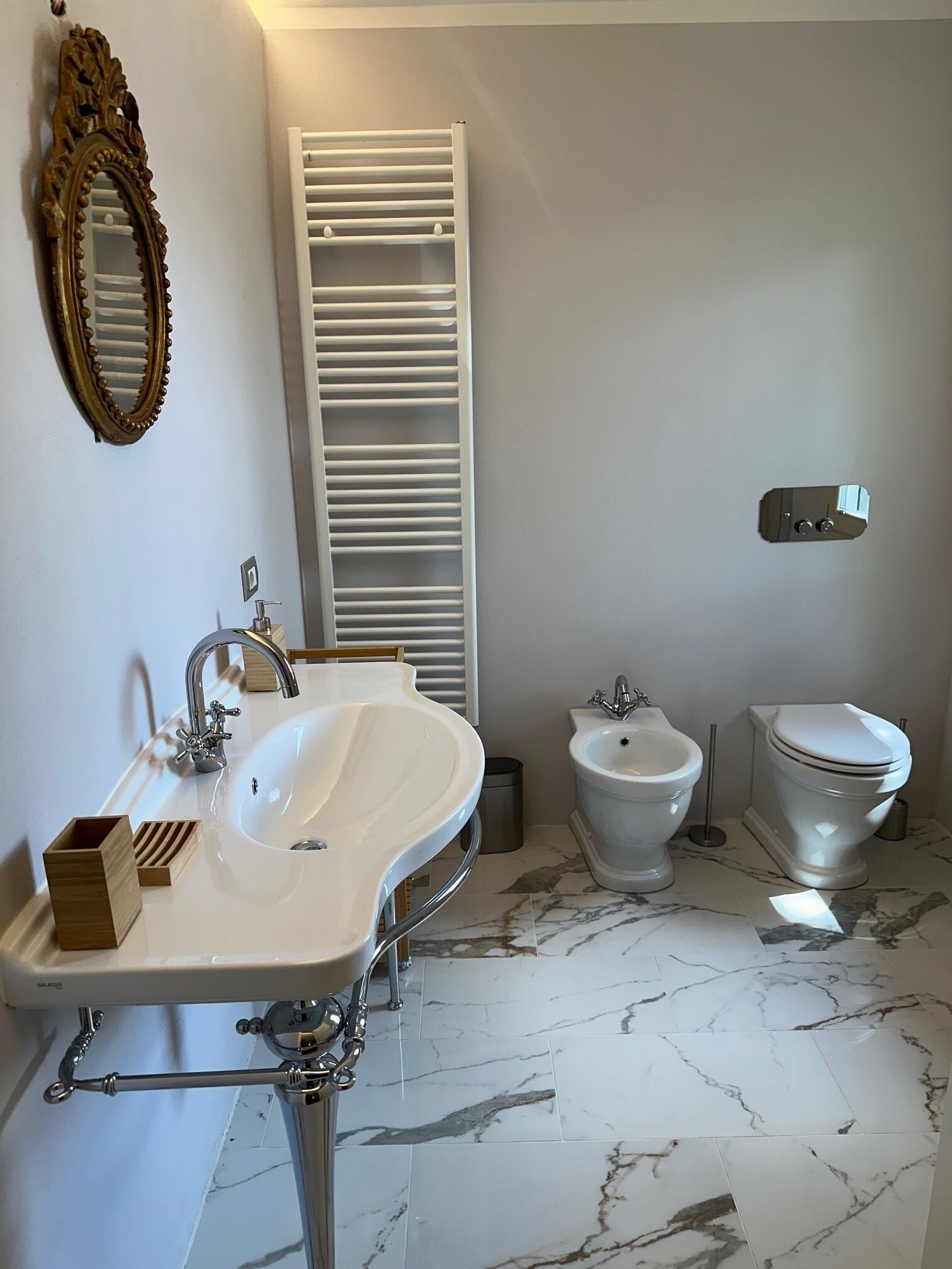 A bathroom with a white sink, bidet, and toilet, marble flooring, and a white towel rack.