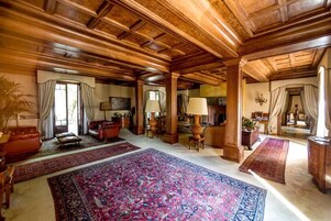 Amplia habitación con techo de madera alto, ventanas grandes con cortinas y un tapete ornamentado de grandes dimensiones.