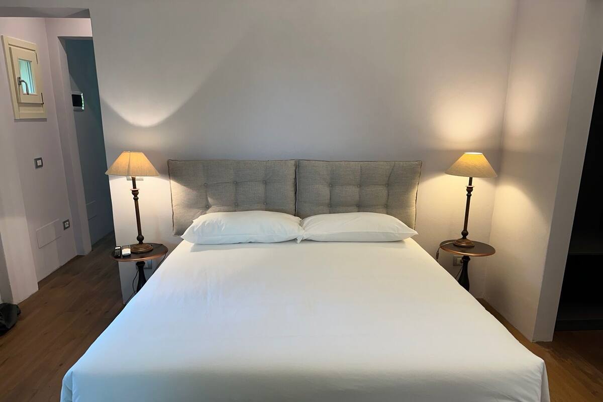 A large bed with a grey upholstered headboard, two bedside lamps, and white bedding.