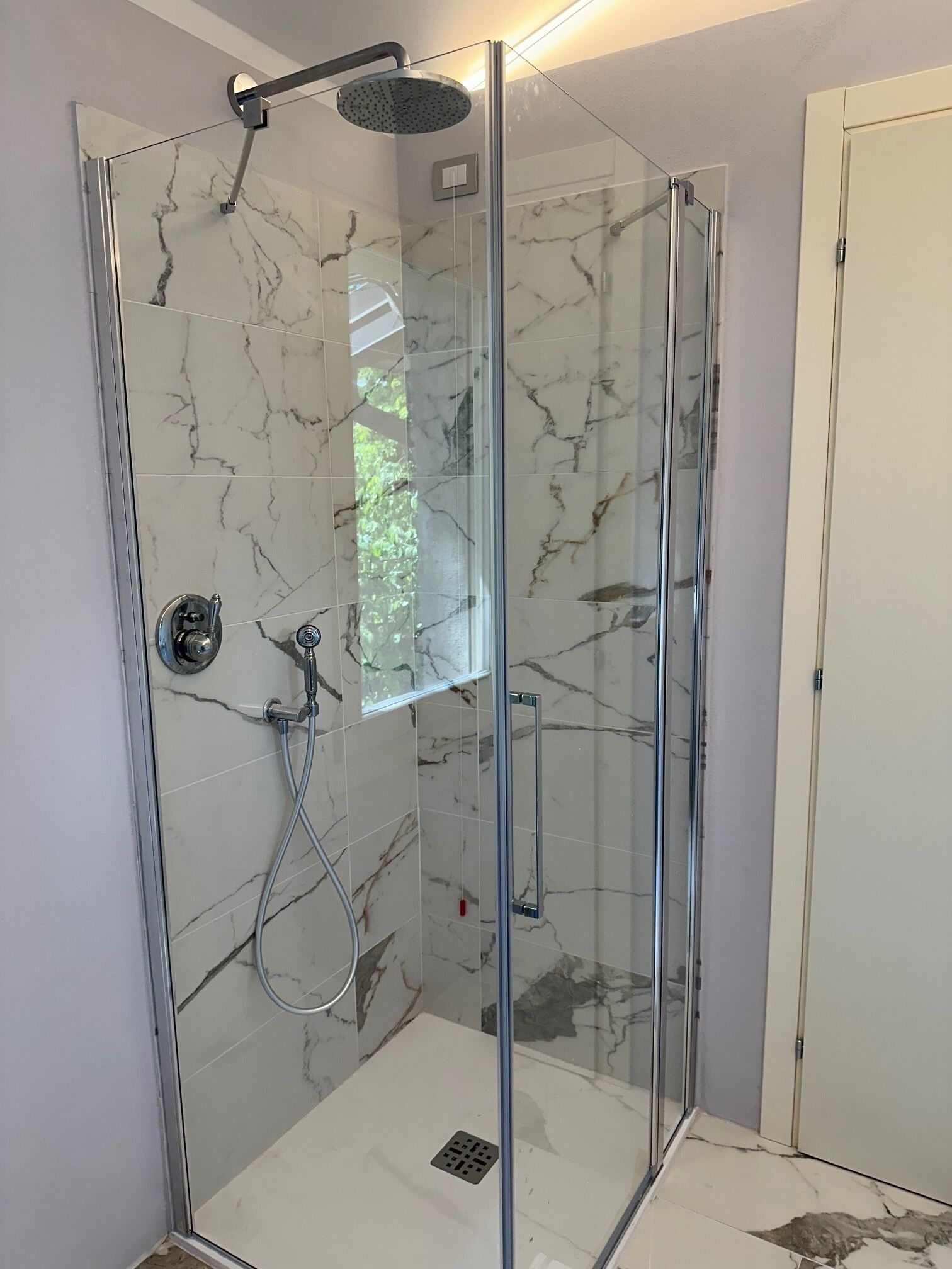 A glass-enclosed shower with a handheld showerhead and a wall-mounted control.