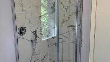 A glass-enclosed shower with a handheld showerhead and a wall-mounted control.