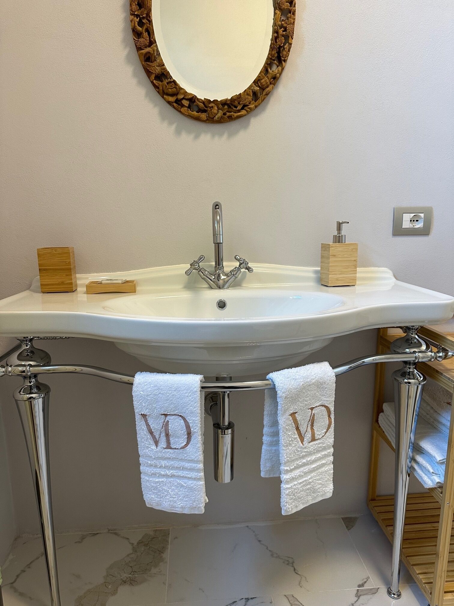A bathroom with a white sink, two towel racks with towels, a wooden soap dispenser, and a decorative mirror.