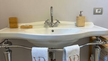A bathroom with a white sink, two towel racks with towels, a wooden soap dispenser, and a decorative mirror.