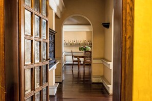 A hallway with a wooden door, a dining area with a table and chairs, and a shelf with glassware. - Villa Dom (Piacenza)