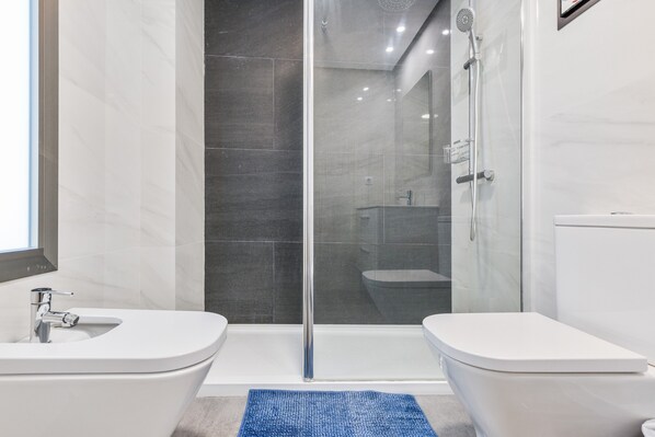 A modern bathroom with a glass-enclosed shower, two sinks, and a toilet.