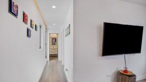 Ein Flur mit einem an der Wand befestigten Flachbildfernseher, einem Holztisch mit Fernbedienung und gerahmten Kunstwerken an der Wand.