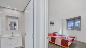 Ein modernes Schlafzimmer mit Bett, einem weißen Kleiderschrank, einem Badezimmer mit Spiegel und Blick auf die Stadt.