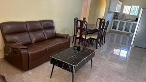 Een zithoek met een bruine leren bank, een salontafel van zwart marmer en een eethoek met houten stoelen en een tafel.