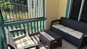 Een balkon met rieten meubilair, waaronder een bank en twee stoelen, en een kleine tafel.