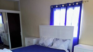 Een slaapkamer met een bed, nachtkastjes, een kledingkast en een raam met gordijnen.