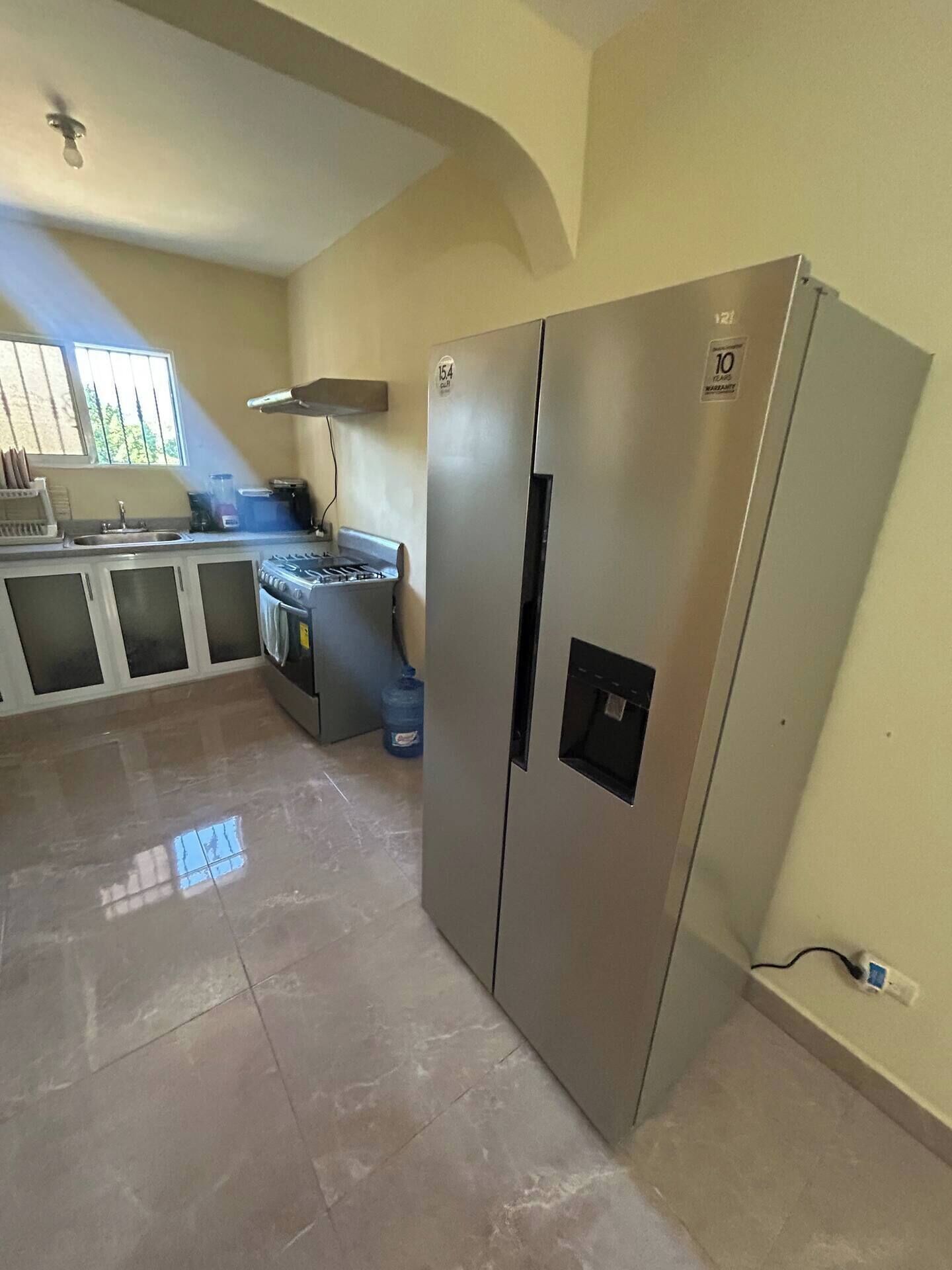 Una cocina con un refrigerador de acero inoxidable, una estufa a gas y un ventanal que proporciona luz natural.
