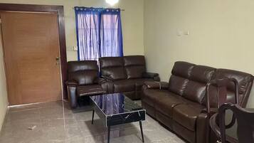 Una sala de estar con un sofá de cuero marrón, una mesa de centro de vidrio y una puerta de madera.