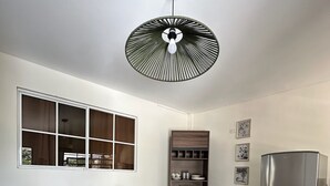 Una cocina moderna con una mesa redonda de madera, sillas negras, un estante empotrado, un refrigerador de acero inoxidable y una lámpara de techo original.