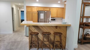 A kitchen with wooden cabinets, a stainless steel refrigerator, a microwave, and a wooden bar stool area. - Snowcreek Resort Vacation Rental 629 (Mammoth Lakes)